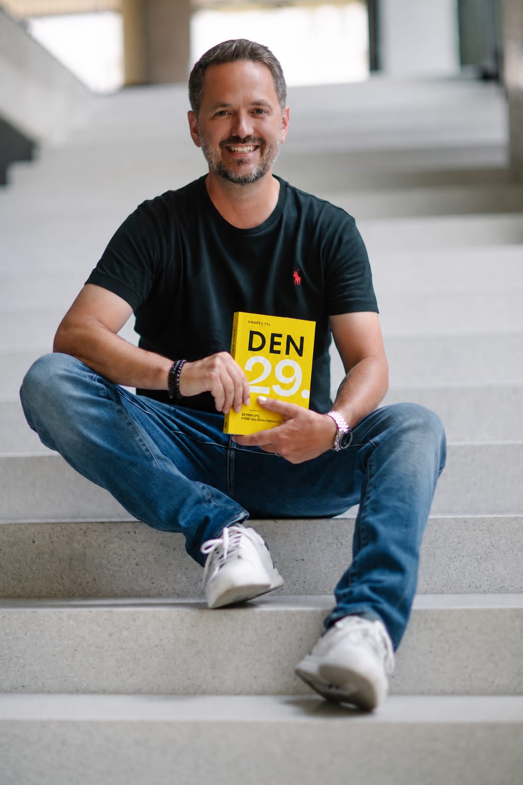 Ondřej Tyl sedí na schodech s knihou Den 29